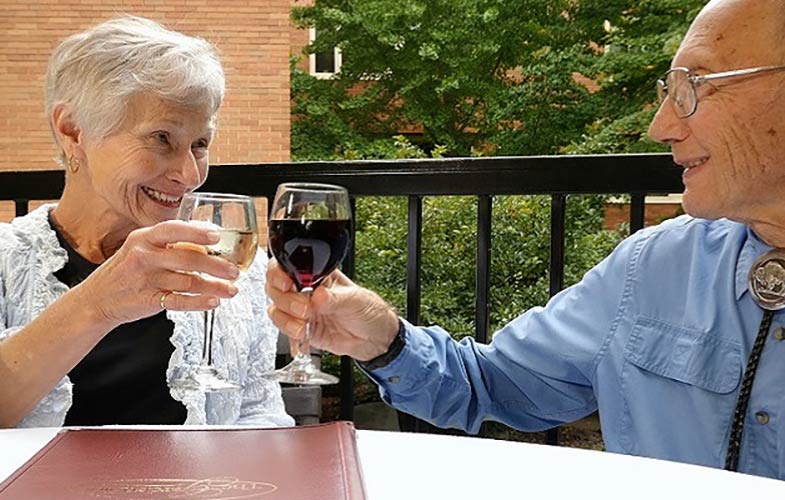 A retired couple with wine on the patio of independent living apartment.